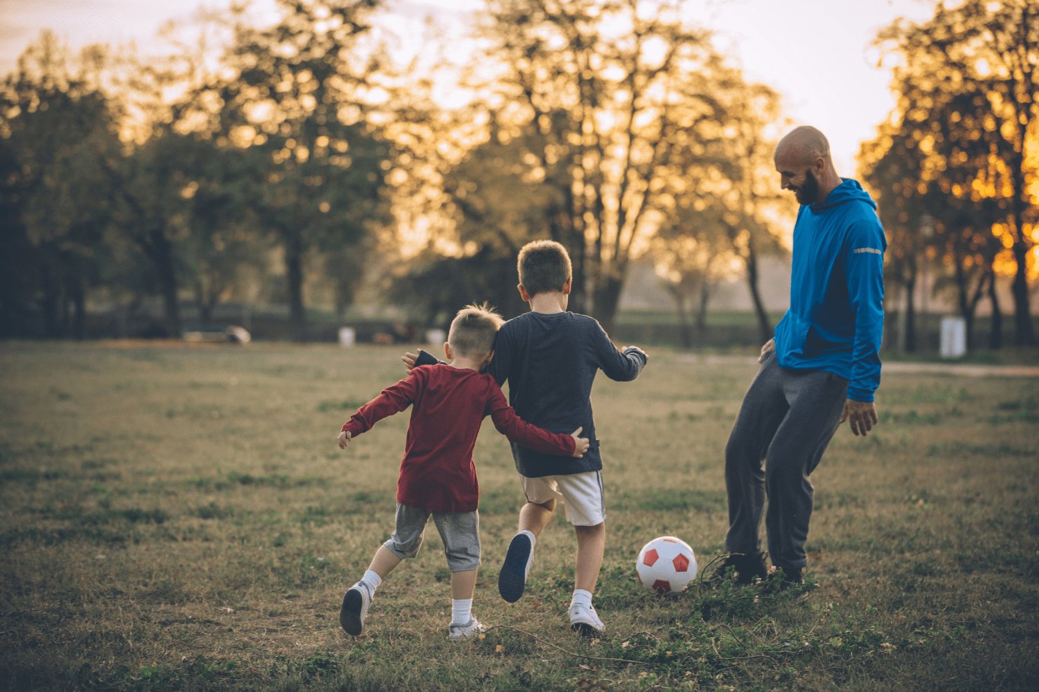 man and children playing football at dusk