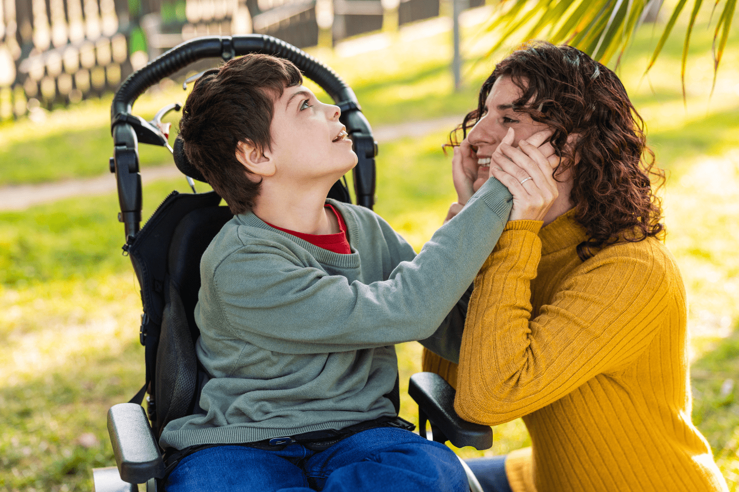 Boy in a wheelchair touching the face of a lady in a yellow jumper